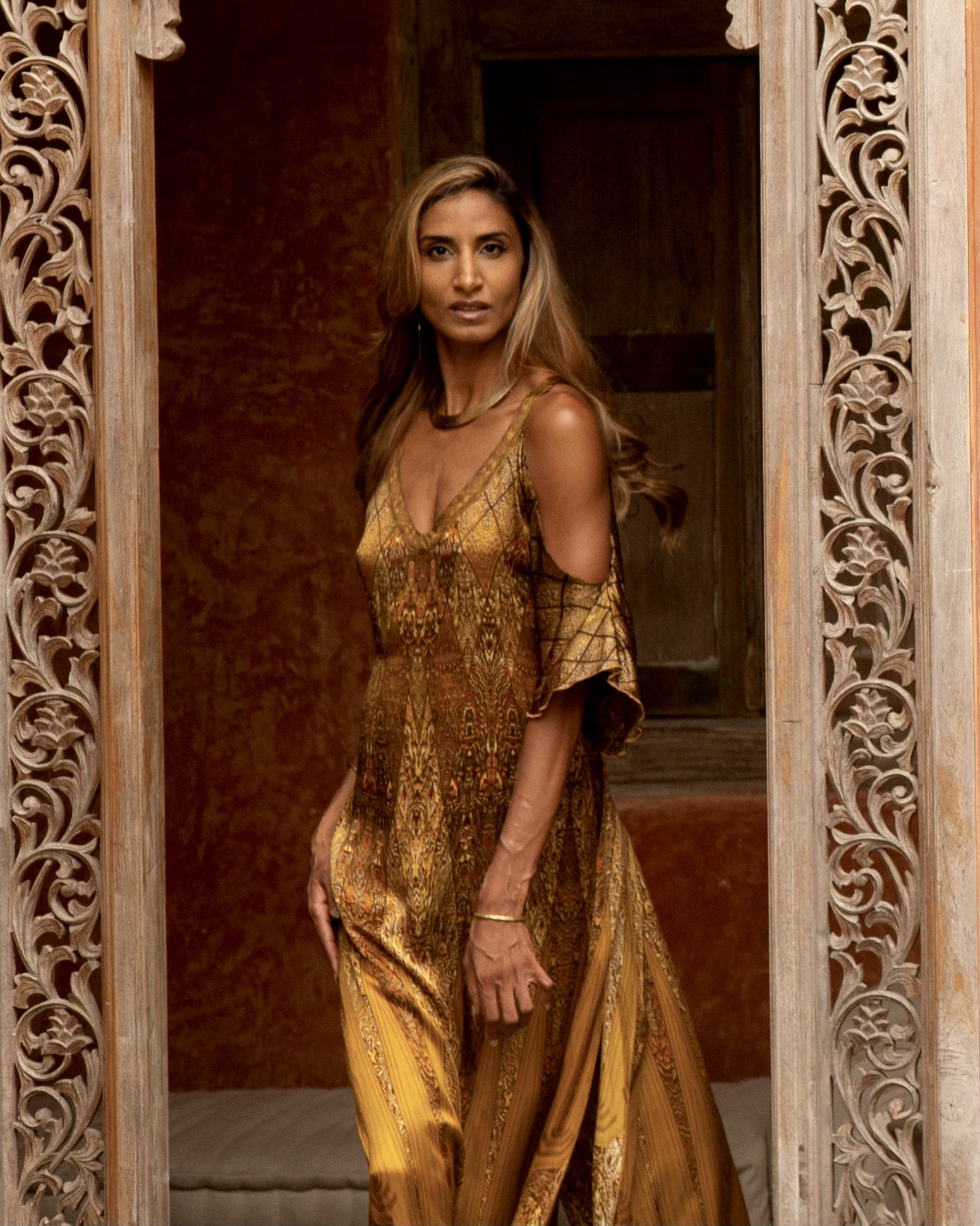 Ruby Noir in a gold gown framed by an ornate doorway